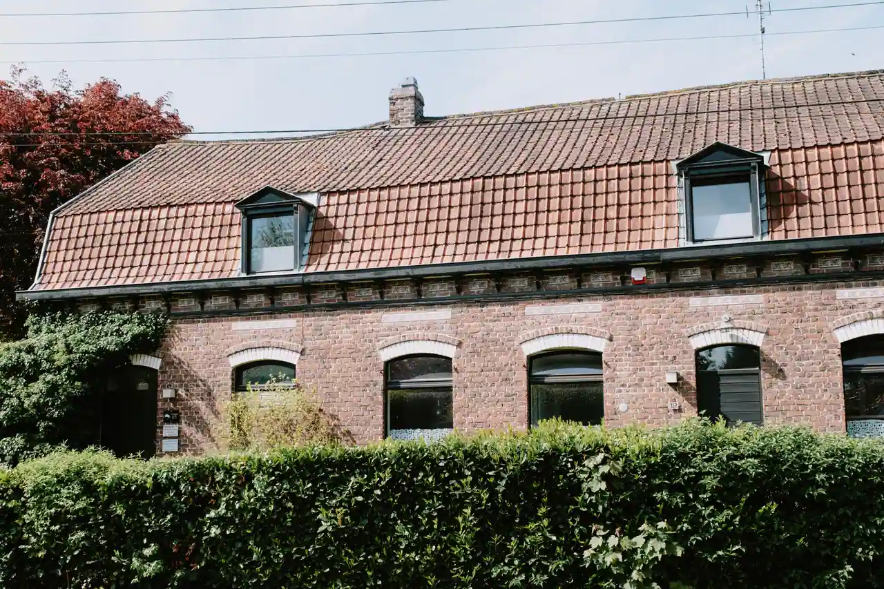 Façade en brique rouge d'une maison mitoyenne du Nord de la France, lucarnes et haie devant l'entrée