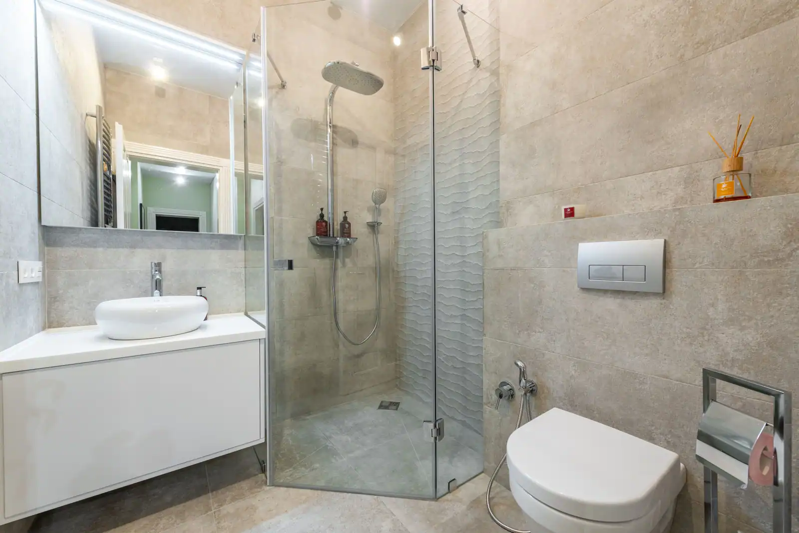Petite salle de bain rénovée : douche d’angle vitrée, meuble suspendu et WC à bâti-support.